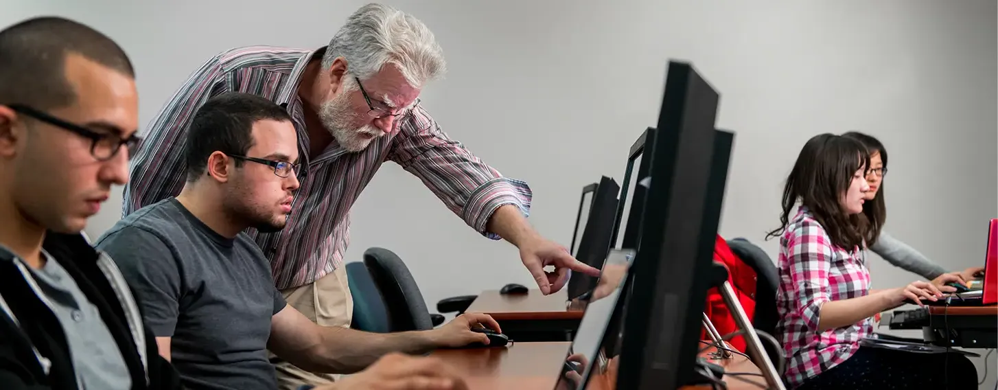 A man instructing students who are using computers in a classroom setting.